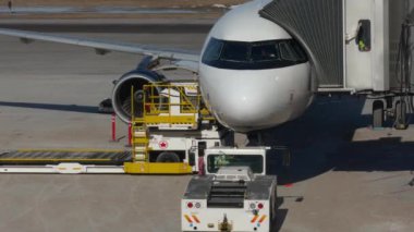 Kapıda park etmiş bir yolcu uçağının 4K 'lık yüksek kalite çekimi ve yolcu bekleyen bir jet köprüsü kolu. Sahne, yer ekibinin uçak bakımı ve...