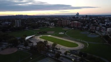 Akşam saatlerinde Halifax 'taki bir şehir parkında uçan bir 4K insansız hava aracı, aşağıdaki beyzbol elmaslarını ve tenis kortlarını yakalıyor. Görüntüler çevredeki yolları gösteriyor. Arabalarla ve şehir manzarası yıkanmış.