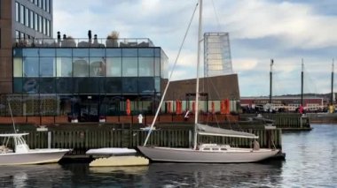 Bulutlu bir sabahta rıhtıma yanaşan yelkenli yatı ve yakınında plastik bir motorlu tekne. Tekne dalgaların üzerinde yavaşça sallanıyor ve gemiler okyanusta görülebiliyor. Yüksek kalite 4K görüntü.