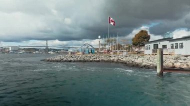 Güneşli bir günde Halifax Feribotundan kalkmak, gemiden gelen dalgalar ve Kanada bayrağını dalgalandırmak. Arkadaki Nova Scotia. Yüksek kalite 4K görüntü.