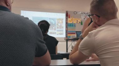 Arka masadan bir dil okulunun içinde 4K 'lık bir çekim. Sınıf, cephedeki öğretmene odaklanmış, öğrenmekle meşgul öğrencilerle dolu. Görüntüler çeşitliliği vurguluyor.