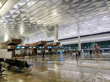 Jakarta, Endonezya 3 Ocak 2024: Geometrik tavan tasarımları, çoklu kontrol gişeleri, parlak katlar ve dağınık yolcular içeren ve temiz ve verimli bir atmosferi yansıtan geniş, modern bir havaalanı terminali.