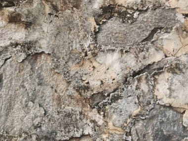 Gri, bej ve kahverengi tonlarında kaba, dokulu bir duvarın yakın çekimi. Yüzey engebeli ve yıpranmış. Karmaşık detaylar ve doğal desenler sergiliyor..