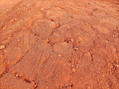 Kırmızımsı kahverengi bir toprak yığını. Kaba bir dokusu var. Doğal manzarayı ve toprağın ham, dokunulmamış şeklini yakalıyor..