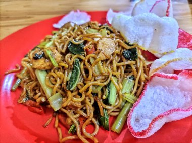 Taze sebzeler ve çıtır krakerlerle kaplı lezzetli bir tabak kızarmış şehriye, canlı kırmızı bir tabakta servis edilir, arzularınızı tatmin etmeye hazır..