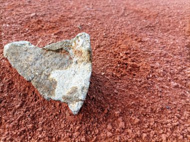 A jagged rock resting on vibrant red soil, capturing natures raw textures and earthy tones. clipart