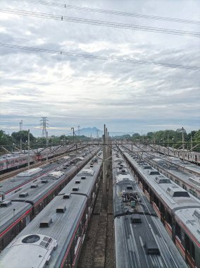 A stunning railway depot filled with countless trains, framed by distant mountains and lush greenery under a dramatic, cloudy sky. clipart