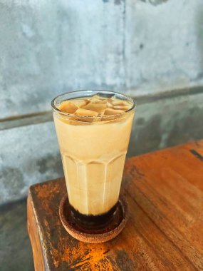 Serinletici bir esmer şekerli buzlu kahve, berrak bir bardakta servis edilir, mükemmel katmanlanmış, sade ahşap arka planlı, rahat titreşimi ayarlayan.