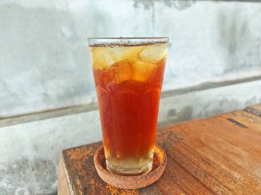 Kırsal ahşap bir masada servis edilen ferahlatıcı bir bardak buzlu çay, basitlik, serinlik ve doğal cazibenin mükemmel bir karışımını yakalıyor..