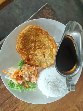 Kızarmış tavuk katsusu, haşlanmış pirinç, ekşi lahana salatası ve soya bazlı sosla servis edilir. Mükemmel bir lezzet uyumu yaratır..