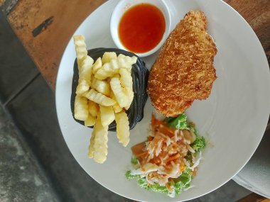 Kızarmış patates ve acı biber sosuyla bezenmiş altın gevrek cordon bleu lezzetli ve doyurucu bir yemek için tabakta servis ediliyor..