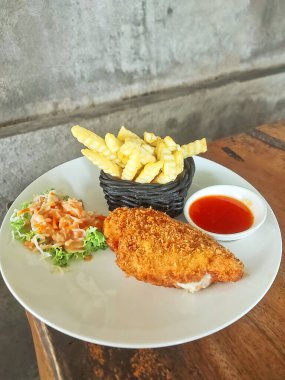 Kızarmış patates, taze salata ve acı biber sosuyla bezenmiş altın, çıtır cordon bleu, tatminkar bir yemek için güzel bir tabakta..