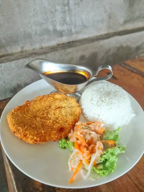 Kızarmış tavuk katsusu, haşlanmış pirinç, ekşi salamura sebze turşusu ve bol baharatlı sos, kırsal ahşap bir masada zarif bir şekilde servis edilir..