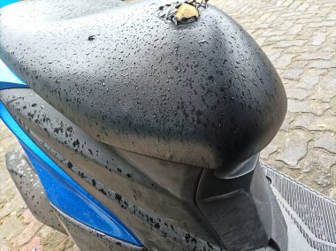 A close-up of a torn motorcycle seat soaked with rainwater, showing detailed droplets and visible damage on the black leather surface. clipart