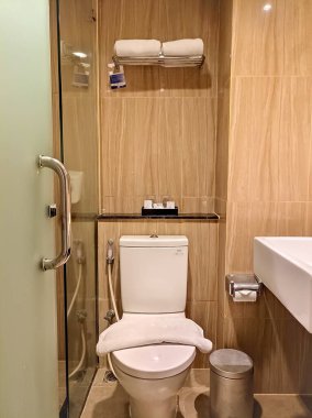 Temiz, modern bir banyo, bej fayanslar, düzgün düzenlenmiş bir tuvalet, cam bir duş kapısı, ve konfor, parlak ve hijyenik bir ortam yaratıyor..