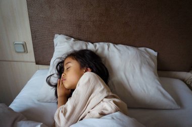 Bir çocuk mışıl mışıl uyurken çekilen huzurlu bir an. Yumuşak yastıklar ve battaniyelerle kucaklanmış. Huzur ve masumiyet saçıyor..