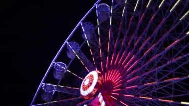 Berrak bir gece gökyüzüne karşı parlak, renkli ışıklarla aydınlatılmış nefes kesici bir dönme dolap.