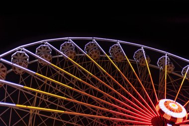 Çarpıcı bir gece fotoğrafı, parlak ışıklarla parlayan bir dönme dolabın büyüleyici bir atmosfer yarattığını gösteriyor.