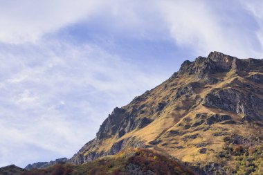 Nefes kesici bir manzara, berrak mavi gökyüzünün altında parlak sonbahar renkleriyle engebeli bir dağın zirvesini yakalar.