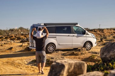 Bir adam çarpıcı bir arazide, doğanın güzelliğini kucaklayarak, minibüsün özgürlüğünden zevk alır.