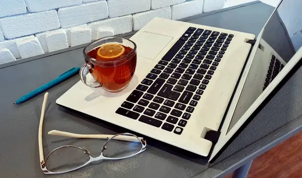 Laptop, çay, bardak ve bir fincan çay.