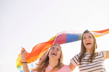 İki kız arkadaş öpüşüyor ve LGBT gurur bayrağı sallıyor..