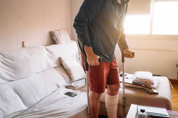 stock image Injured man with bandaged foot walking at home with walking sticks.