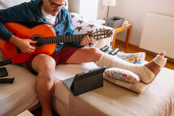 Ranny Człowiek Bandażowaną Stopą Nauczyć Się Grać Gitarze Online — Zdjęcie stockowe
