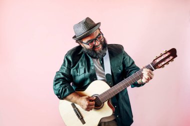 Mutlu sakallı adam pembe arka planda akustik gitar çalıyor..