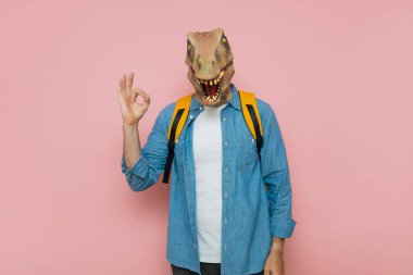 Sırt çantalı ve pembe arka planda kertenkele maskeli bir adam..