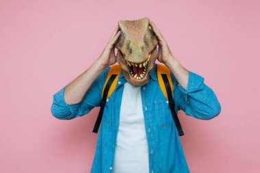 Sırt çantalı ve pembe arka planda kertenkele maskeli bir adam..