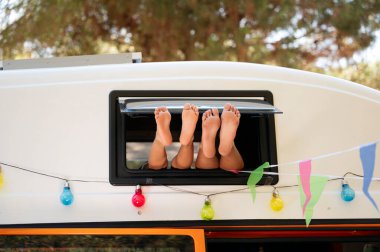 The children's feet stick out the window of the van on a wonderful day of camping. Vanlife concept. clipart