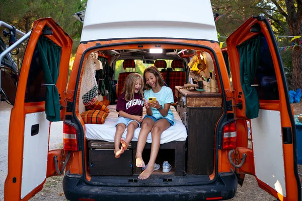 Two sibling boys using the smartphone on a wonderful day camping in a van. Van life concept.