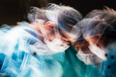 Motion photography with slow exposure of the doctor with mask doing a surgery. Emergency effect.