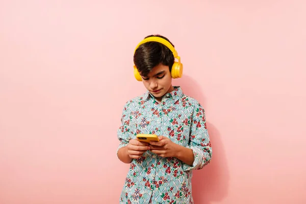 Młody Facet Korzystający Smartfona Żółtych Słuchawek Studio Różowym Tle — Zdjęcie stockowe