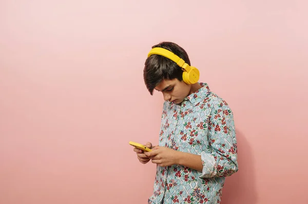 Młody Facet Korzystający Smartfona Żółtych Słuchawek Studio Różowym Tle — Zdjęcie stockowe