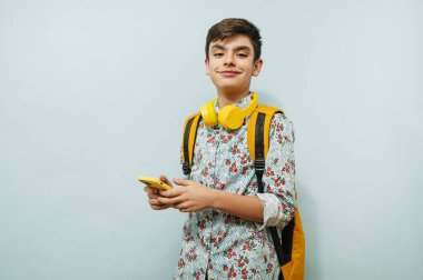 Stüdyoda mavi arka planda akıllı telefon ve sarı kulaklık kullanan genç adam..