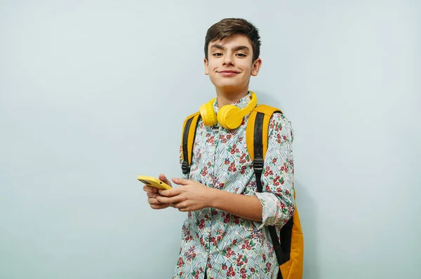 Νεαρός Που Χρησιμοποιεί Smartphone Και Κίτρινα Ακουστικά Στο Στούντιο Μπλε — Φωτογραφία Αρχείου