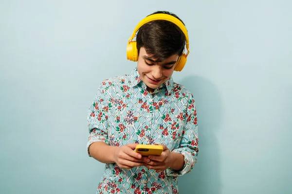 Stüdyoda Mavi Arka Planda Akıllı Telefon Sarı Kulaklık Kullanan Genç — Stok fotoğraf