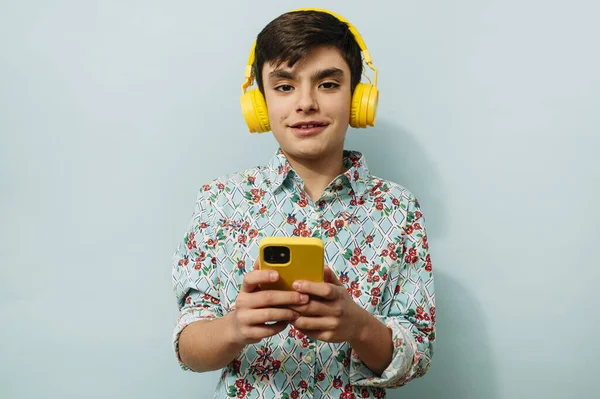 Νεαρός Που Χρησιμοποιεί Smartphone Και Κίτρινα Ακουστικά Στο Στούντιο Μπλε — Φωτογραφία Αρχείου
