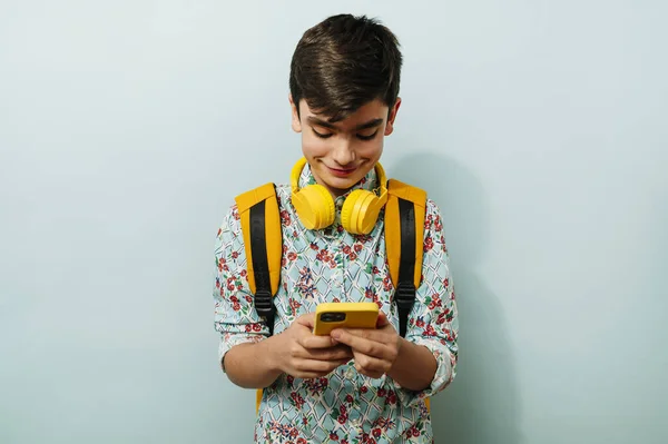 Stüdyoda Mavi Arka Planda Akıllı Telefon Sarı Kulaklık Kullanan Genç — Stok fotoğraf