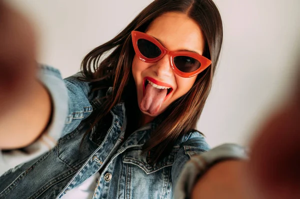 Close up of a beautiful woman with her tongue out taking photos with a smartphone, selfie.