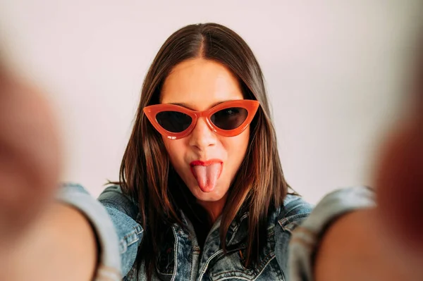 Close up of a beautiful woman with her tongue out taking photos with a smartphone, selfie.