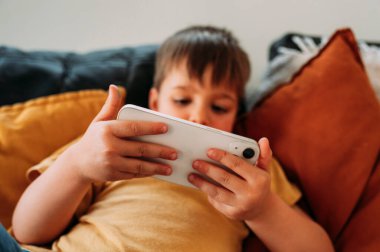 Kanepede uzanmış akıllı telefon kullanan çocuk...