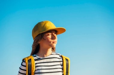 Sarışın, güzel bir kadının açık hava portresi. Sarı şapkalı ve dişlerinde bir deste var..