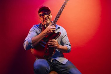 Kırmızı arkaplanda elektro gitar çalan adam