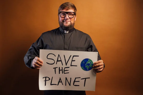 Portrait of a priest with a crucifix holding a sign that says SAVE THE PLANET.