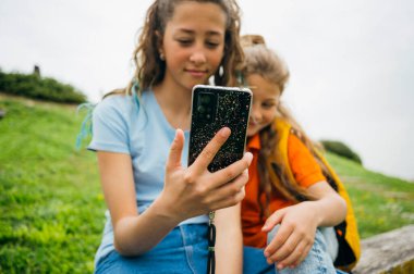 Bahçede oturan akıllı telefonu kullanan ablası tarafından eşlik edilen bir çocuk..