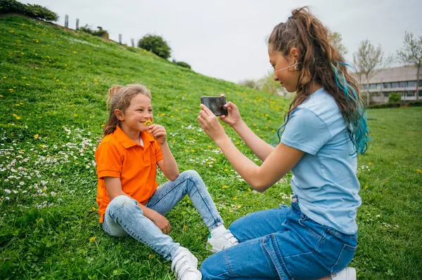 Bahçede oturan akıllı telefonu kullanan ablası tarafından eşlik edilen bir çocuk..