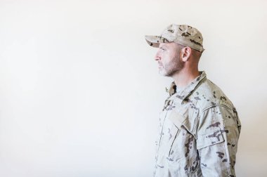 Kamuflajlı ordu üniformalı beyaz adam kollarını kavuşturuyor.